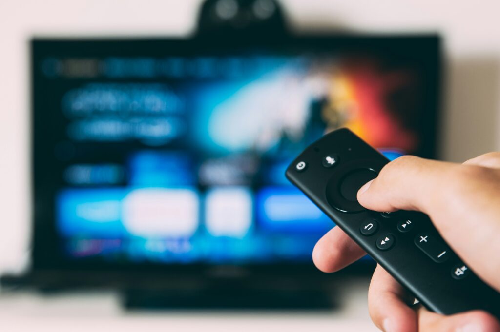 person holding a TV remote pointing at a TV with blurred background