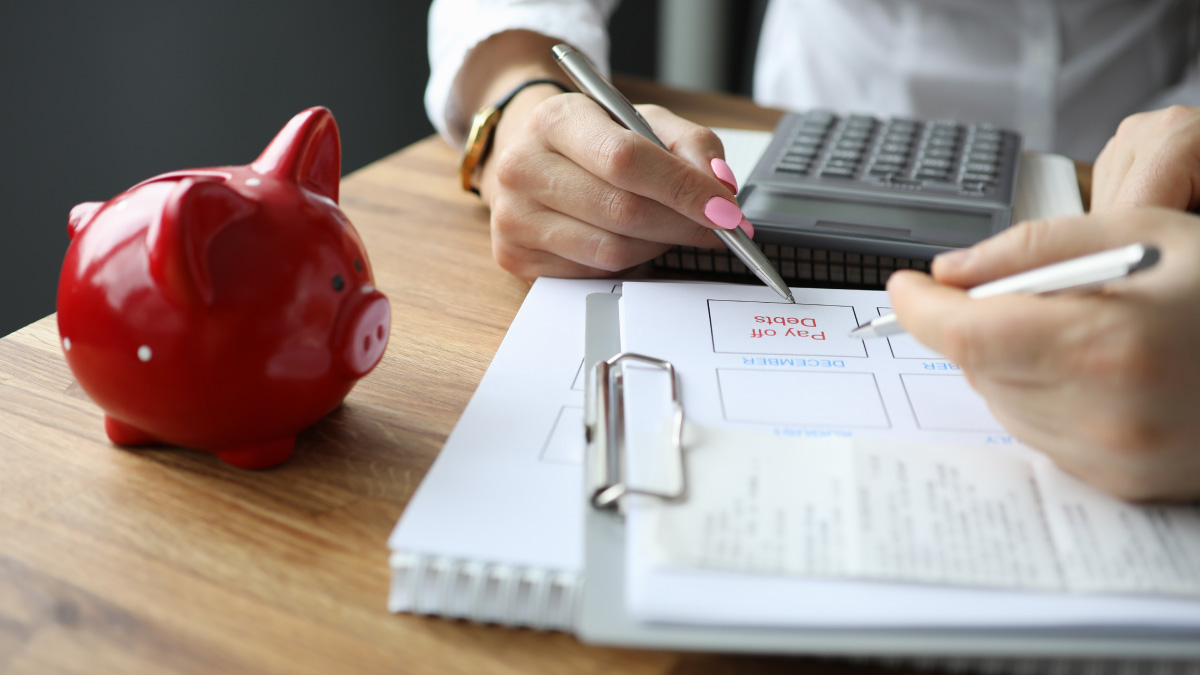 image of someone writing on a notepad next to a piggy bank